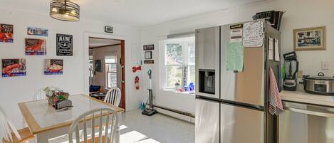 A kitchen with a stainless steel refrigerator, a dining table with chairs, and various wall decorations including signs and a framed picture.
