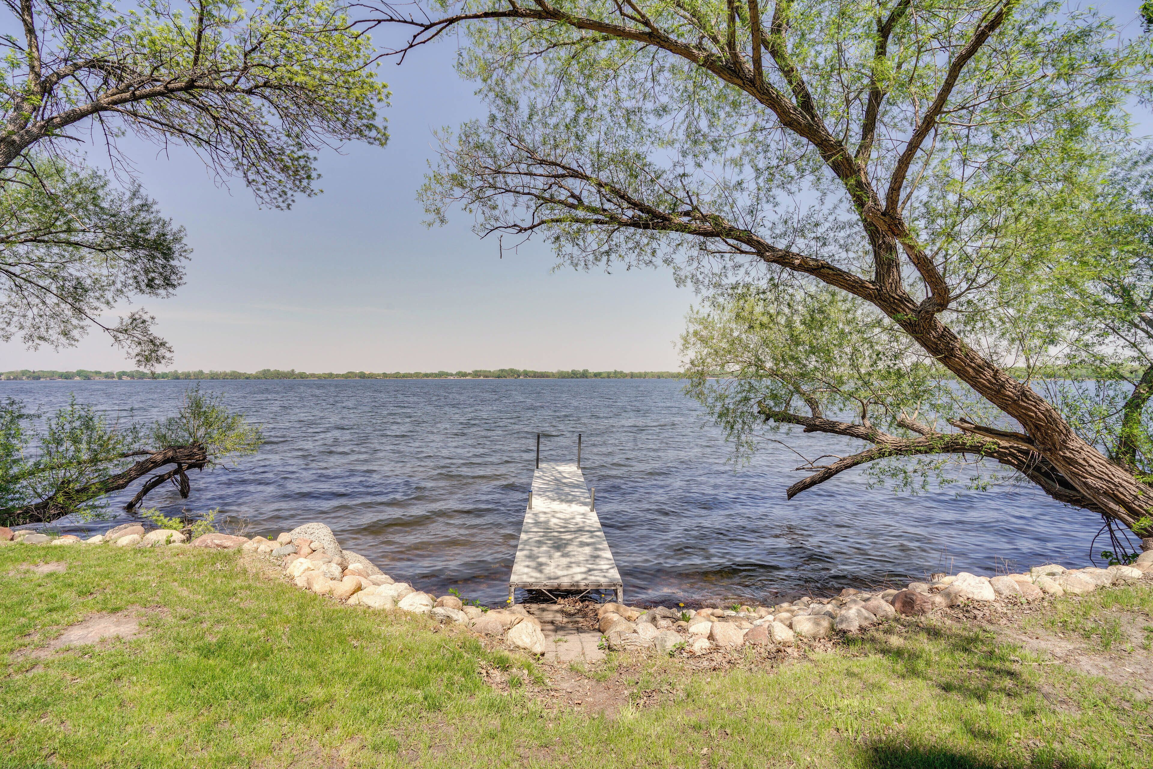 A wooden dock extending into a calm lake, surrounded by a stone wall and lush greenery.