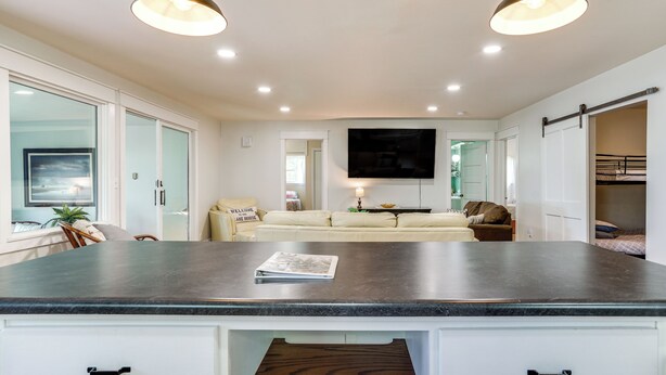 A modern kitchen with a dark countertop, white cabinetry, and a built-in wooden drawer. - Lakeside Litchfield Home w/ Patio & Gas Grill! (Litchfield)