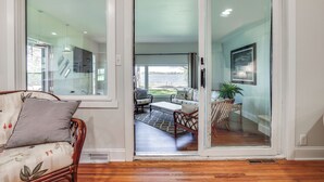 A modern interior with a wooden floor, a sofa with a floral pattern, and a sliding glass door leading to a balcony with outdoor furniture. - Lakeside Litchfield Home w/ Patio & Gas Grill! (Litchfield)