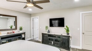 Ein Schlafzimmer mit Bett, Schminktisch, Fernseher und Deckenventilator.