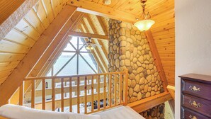 A high-ceilinged wooden room with a sloped roof, a stone wall, and a wooden railing. - Upper Peninsula Lakefront A-frame Cabin w/ Dock (Channing)