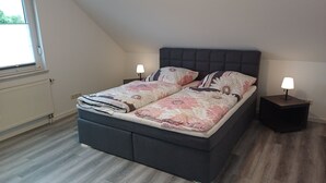 Une chambre à coucher avec un lit, deux tables de chevet, une fenêtre et un radiateur.