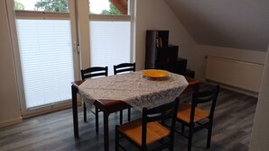 Un coin repas avec une table recouverte d’une nappe en dentelle, quatre chaises en bois et un bol jaune posé sur la table.