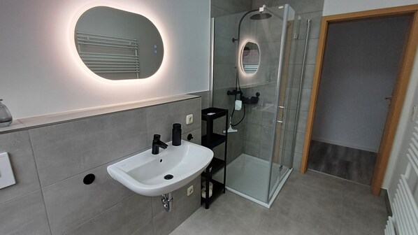 Une salle de bain moderne avec un lavabo blanc, une douche en verre et une porte en bois.