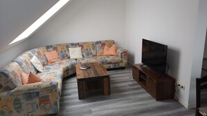 Une chambre de style loft moderne avec un plafond en pente, un canapé d’angle agrémenté de coussins à motifs, une table basse en bois, un téléviseur posé sur un meuble en bois et une armoire intégrée.