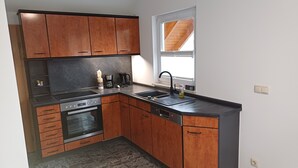 Une cuisine compacte avec des meubles en bois, un four encastré, une plaque de cuisson et un évier.