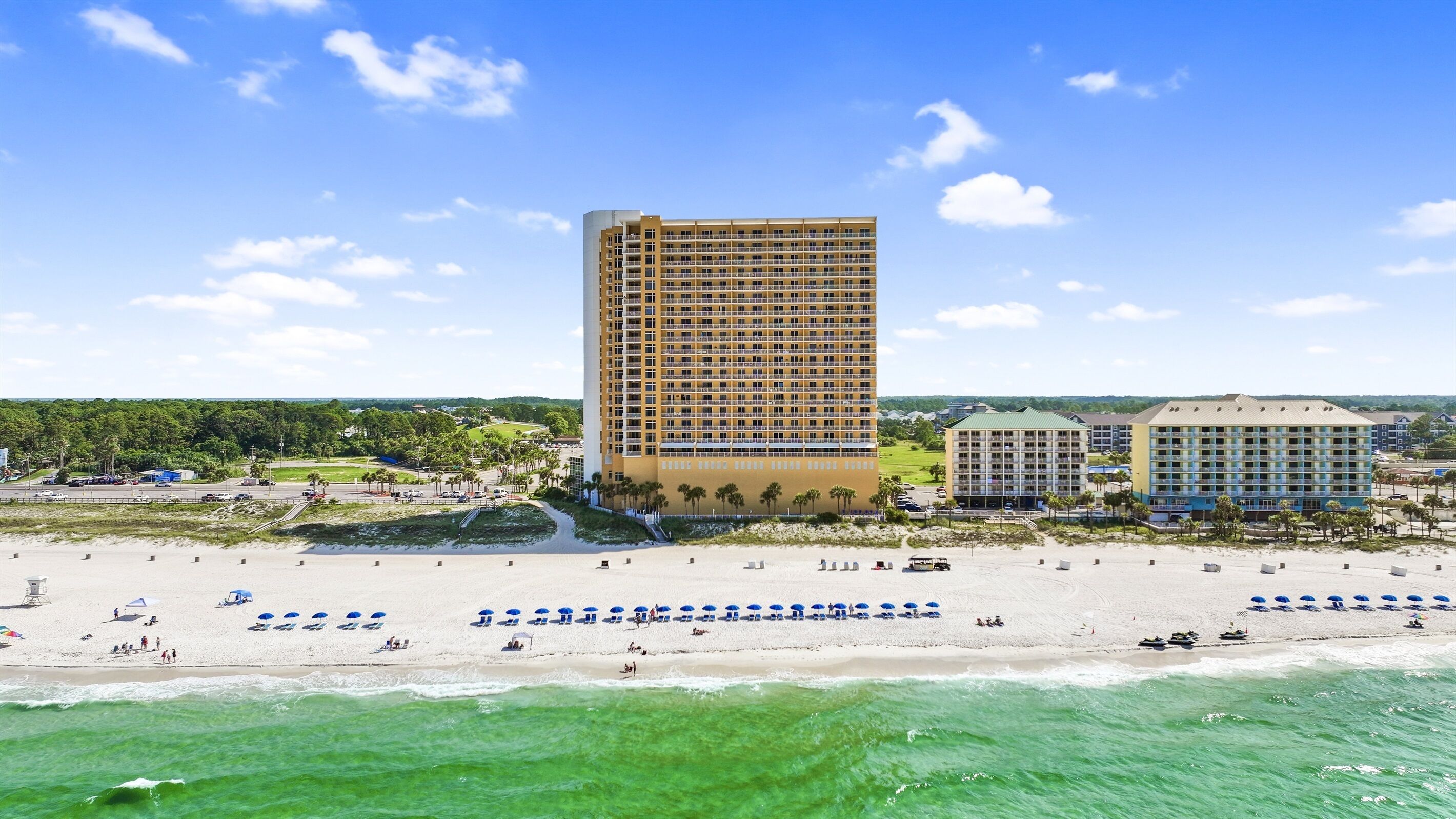 A beachfront hotel with multiple buildings, a sandy beach with umbrellas, and ocean views.