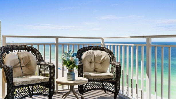 A balcony with wicker chairs and a small table, overlooking a beach and ocean. - Panoramic Sunset Views, Beachfront (Panama City Beach)