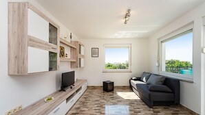 A modern living room with a flat-screen TV, a dark sofa, and a large window offering a view of greenery. - Gorgeous home in Polaca (Polaca)