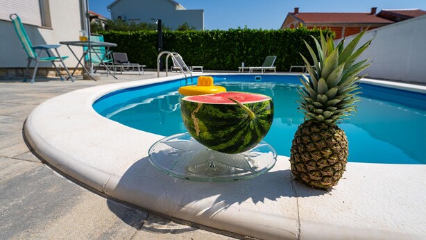 A swimming pool with a glass bowl containing a watermelon and a pineapple on the edge. - Gorgeous home in Polaca (Polaca)