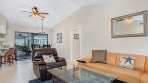 A living room with a glass coffee table, leather sofas, a ceiling fan, and a dining area with chairs. - Waterfront Paradise Heated Pool, Dock, Grill, Fishing near restaurants and shops (Punta Gorda)
