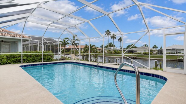 A swimming pool with a glass enclosure, surrounded by palm trees and a clear sky. - Waterfront Paradise Heated Pool, Dock, Grill, Fishing near restaurants and shops (Punta Gorda)