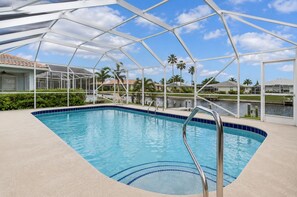 Une piscine entourée de palmiers, protégée par une paroi de verre et surplombée d’un ciel dégagé.