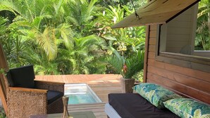 A covered outdoor seating area with a pool, wooden furniture, and lush greenery in the background. - Cottage in the heart of the rainforest  (Sainte-Rose)