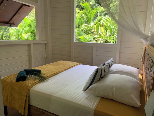 A single bed with a yellow blanket, white pillows, and a dark blue towel. - Vacation Home in the Heart of the Rainforest (Sainte-Rose)