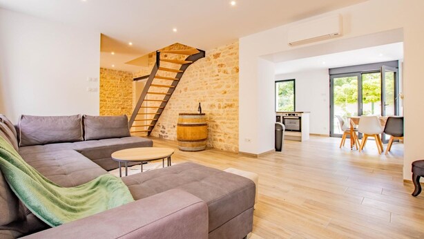 A modern living room with a stone accent wall, a staircase, a sofa, and a dining area with natural light.