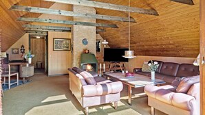Ein gemütliches Wohnzimmer im Loft-Stil mit freiliegenden Holzbalken, einem Kamin, Ledersofas und einem Flachbildfernseher.