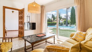 A living room with a TV, a sofa, a coffee table, and a view of a pool and greenery. - Stunning home in Vélez-Málaga (Vélez-Málaga)