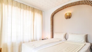 A bedroom with two beds, a curved brick wall, a wall-mounted light fixture, and sheer curtains. - Stunning home in Vélez-Málaga (Vélez-Málaga)