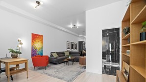 A modern living room with a grey sofa, red armchair, and a colorful abstract painting. - New Modern 2bdr Apartment in Little Italy (Montréal)