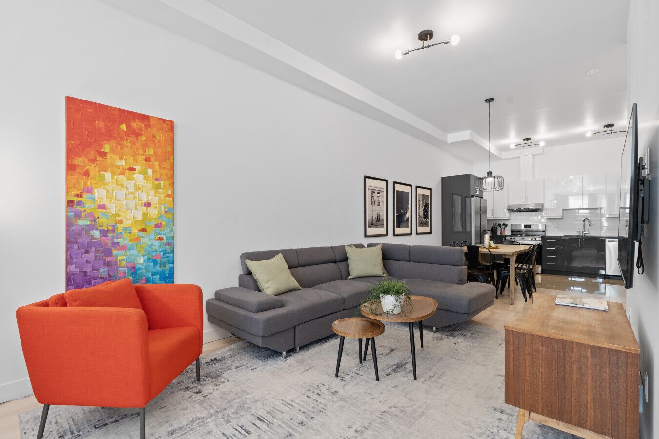 A modern living room with a gray sofa, orange armchair, and a colorful abstract painting.