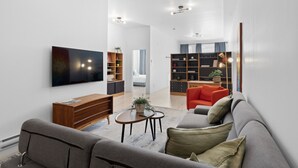 A modern living room with a flat-screen TV, a sofa, a coffee table, and a bookshelf. - New Modern 2bdr Apartment in Little Italy (Montréal)