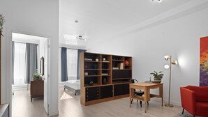 A modern living room with a wooden bookshelf, a red armchair, a small table, and a floor lamp. - New Modern 2bdr Apartment in Little Italy (Montréal)