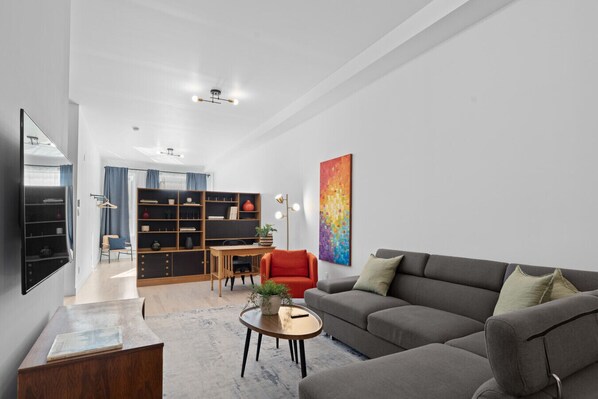 A modern living room with a grey sofa, a red chair, a wooden coffee table, and a bookshelf. - New Modern 2bdr Apartment in Little Italy (Montréal)