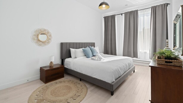 A modern bedroom with a bed, bedside table, lamp, and a decorative mirror. - New Modern 2bdr Apartment in Little Italy (Montréal)