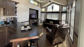 A modern kitchen with a built-in oven, a coffee maker, and a TV. There is a dining area with a bar counter and a sofa. - WALK TO INDIAN RIVER MARINA AT NORRIS LAKE
Book now! Memorial Weekend available (Jacksboro)