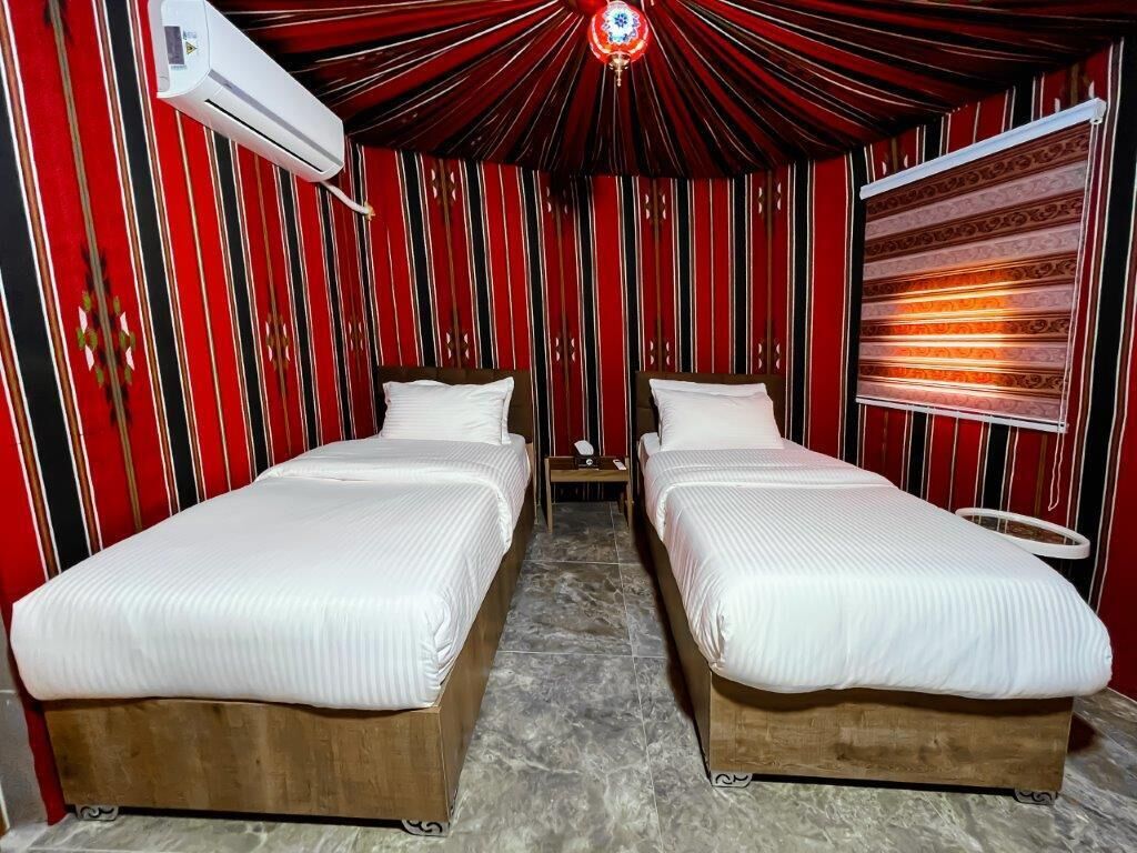 Una stanza con due letti di legno, una parete a righe rosse, una ventola a soffitto e un condizionatore d'aria.
