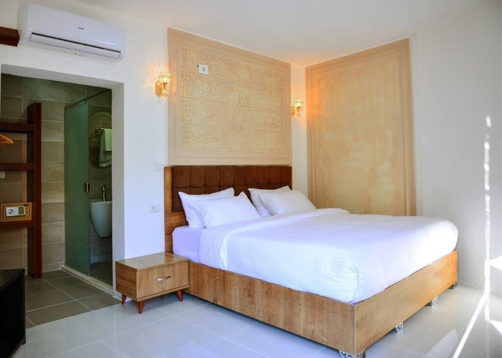 Una camera da letto con un letto in legno, un comodino, un condizionatore d'aria a muro e un bagno con box doccia in vetro.