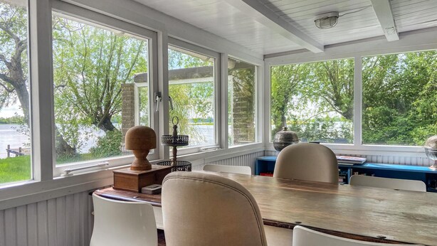 A sunroom with large windows, a wooden table, and white chairs. - Stunning (sta)caravan in Reeuwijk (Reeuwijk)