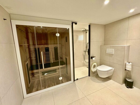 Un baño moderno con ducha de vidrio, inodoro y cubo de basura.