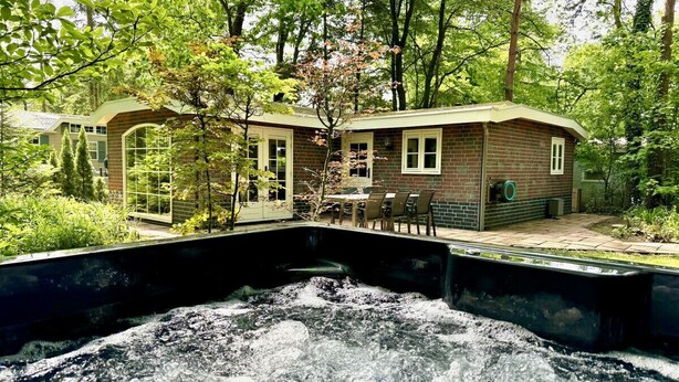 Un chalet rustique doté d’un bain à remous, entouré d’une végétation luxuriante et d’arbres.