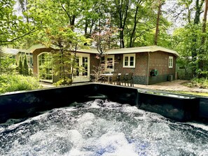 Una cabaña rústica con jacuzzi rodeada de exuberante follaje y árboles.