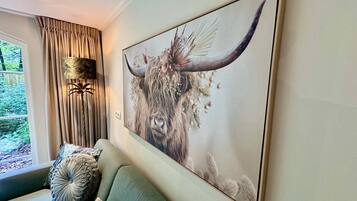 A living room with a large wall-mounted artwork of a bull, a sofa with cushions, a floor lamp, and a window with curtains.