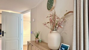 Une pièce comprenant un meuble en bois, un grand vase contenant des fleurs séchées, une tablette et une horloge murale.