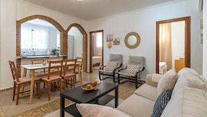 A living room with a sofa, two armchairs, a dining table with chairs, and a kitchen area with a window. - Gorgeous apartment in Malaga with house sea view (Malaga)
