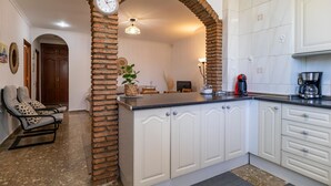 A kitchen with white cabinets, a brick column, a clock, and a coffee maker. - Gorgeous apartment in Malaga with house sea view (Malaga)