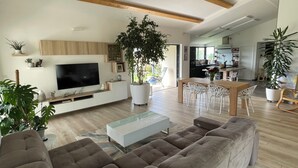 Una sala de estar moderna con una televisión de pantalla plana, una planta grande en maceta, un sofá y un comedor con sillas.