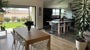 Una cocina moderna con una isla central, sillas blancas y una mesa de comedor con un jarrón de flores.