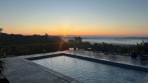 Una piscina con vistas al atardecer, rodeada por un patio con sillas y una mesa.
