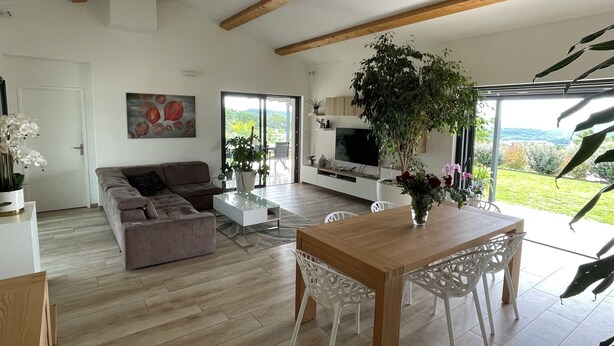 Una sala de estar moderna con un sofá, una mesa de centro y una mesa de comedor con sillas. Hay un televisor y un ventanal con vistas al exterior.