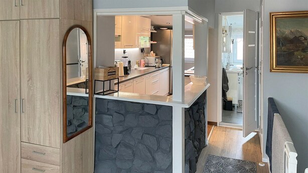 Cocina moderna con una isla de piedra, armarios de madera y vistas al baño contiguo.