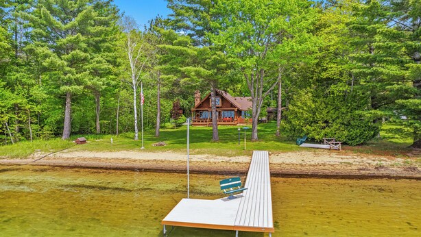 Une jetée en bois s’étendant dans une étendue d’eau claire, avec un banc, entourée d’arbres verdoyants et une cabane en arrière-plan.