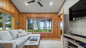 Un salon moderne avec un intérieur en bois, un grand téléviseur à écran plat et une vue sur l’extérieur.