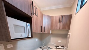 A modern kitchen with wooden cabinets, a built-in microwave, and a stainless steel sink. - Mini Suite Equipada Frente al Aeropuerto! (Guayaquil)