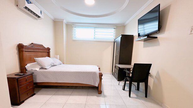 A bedroom with a bed, a desk, a chair, a TV, and a wardrobe. - Mini Suite Equipada Frente al Aeropuerto! (Guayaquil)